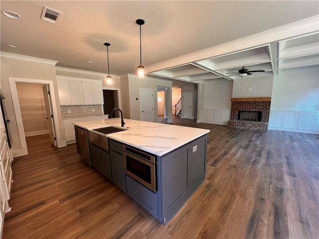 kitchen featuring dark hardwood / wood-style floors, a center island with sink, a brick fireplace, pendant lighting, and white cabinetry