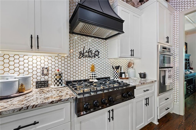 kitchen with tasteful backsplash, appliances with stainless steel finishes, custom range hood, light stone countertops, and white cabinets