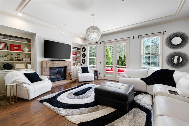 living room featuring built in features, a fireplace, a tray ceiling, dark wood-type flooring, and french doors