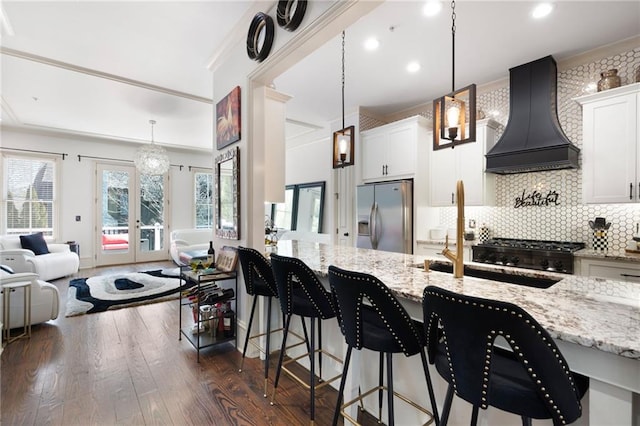 kitchen featuring decorative light fixtures, a kitchen breakfast bar, stainless steel fridge, custom range hood, and white cabinets