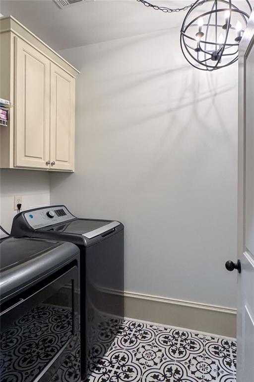 laundry area featuring a notable chandelier, tile patterned floors, cabinets, and washing machine and clothes dryer