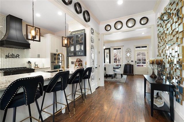 kitchen featuring custom exhaust hood, white cabinetry, tasteful backsplash, decorative light fixtures, and light stone countertops