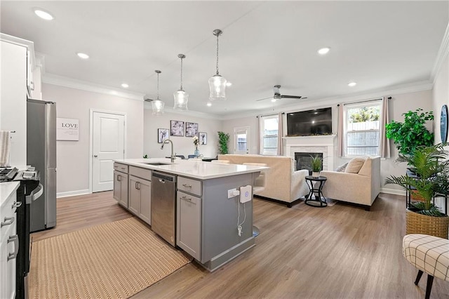 kitchen with sink, gray cabinetry, ornamental molding, appliances with stainless steel finishes, and a kitchen island with sink