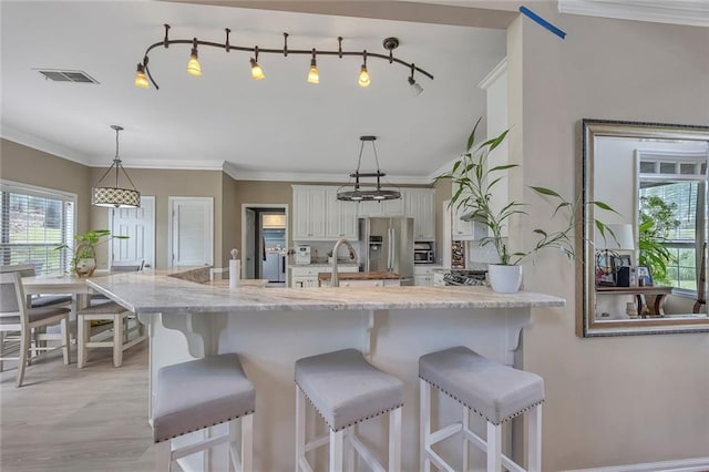 225 Ruby Forest Pkwy, Suwanee, GA 30024 - kitchen featuring stainless steel fridge, healthy amount of natural light, white cabinets, a kitchen breakfast bar, and crown molding