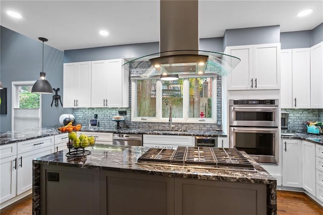 kitchen featuring white cabinetry, island exhaust hood, dark stone counters, a kitchen island, and appliances with stainless steel finishes