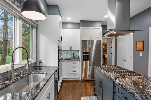 kitchen with dark stone counters, white cabinets, sink, island exhaust hood, and stainless steel appliances