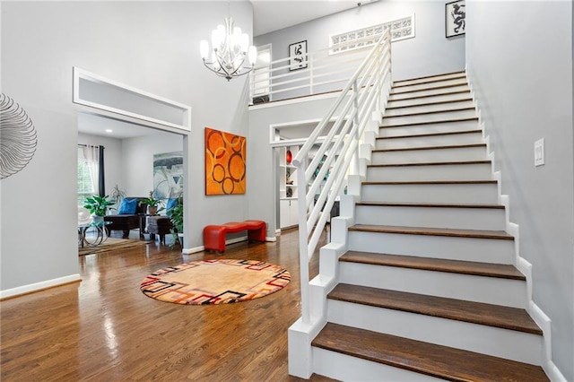 stairway featuring a towering ceiling, hardwood / wood-style flooring, and an inviting chandelier