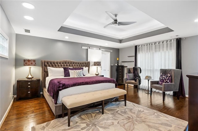 bedroom with a barn door, a tray ceiling, ceiling fan, and dark hardwood / wood-style floors