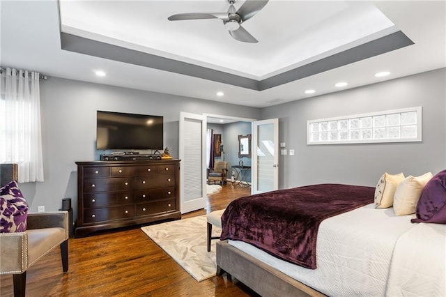 bedroom with ceiling fan, dark hardwood / wood-style floors, and a raised ceiling