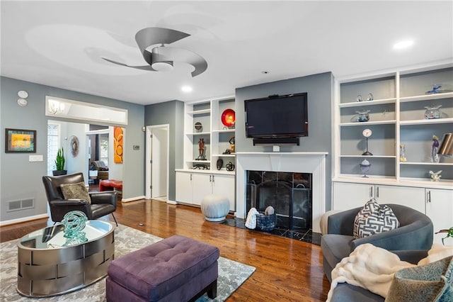 living room with a fireplace, hardwood / wood-style floors, built in features, and ceiling fan