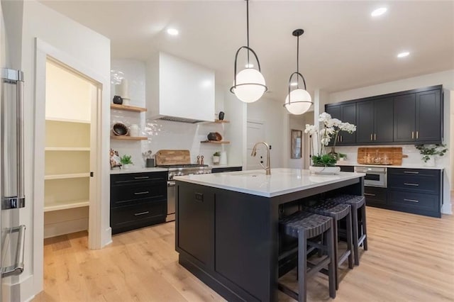 kitchen with sink, hanging light fixtures, light hardwood / wood-style floors, stainless steel stove, and custom exhaust hood