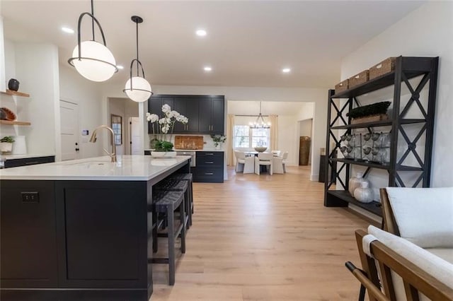 kitchen with sink, light hardwood / wood-style flooring, decorative light fixtures, a kitchen bar, and a center island with sink