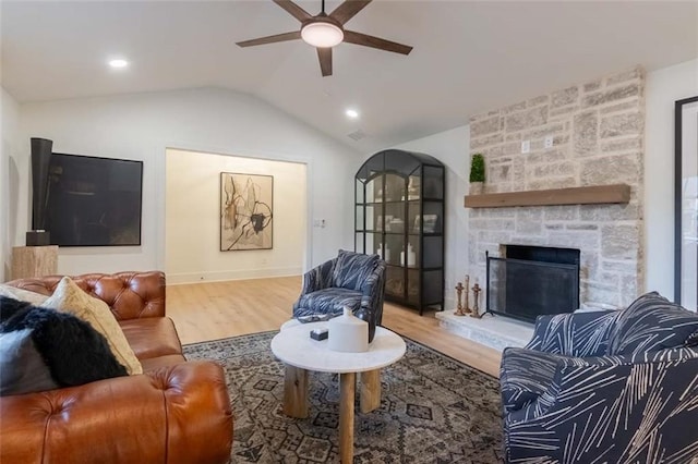 living room featuring hardwood / wood-style flooring, a stone fireplace, ceiling fan, and lofted ceiling