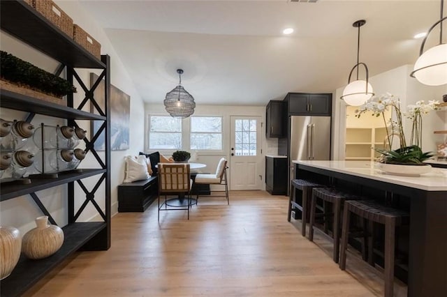 kitchen featuring light hardwood / wood-style floors, vaulted ceiling, decorative light fixtures, high quality fridge, and a breakfast bar