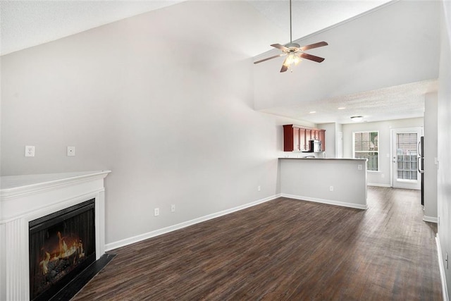 222 Ben Ln, Fairburn, GA 30213 - unfurnished living room with dark wood-style floors, ceiling fan, a lit fireplace, baseboards, and lofted ceiling