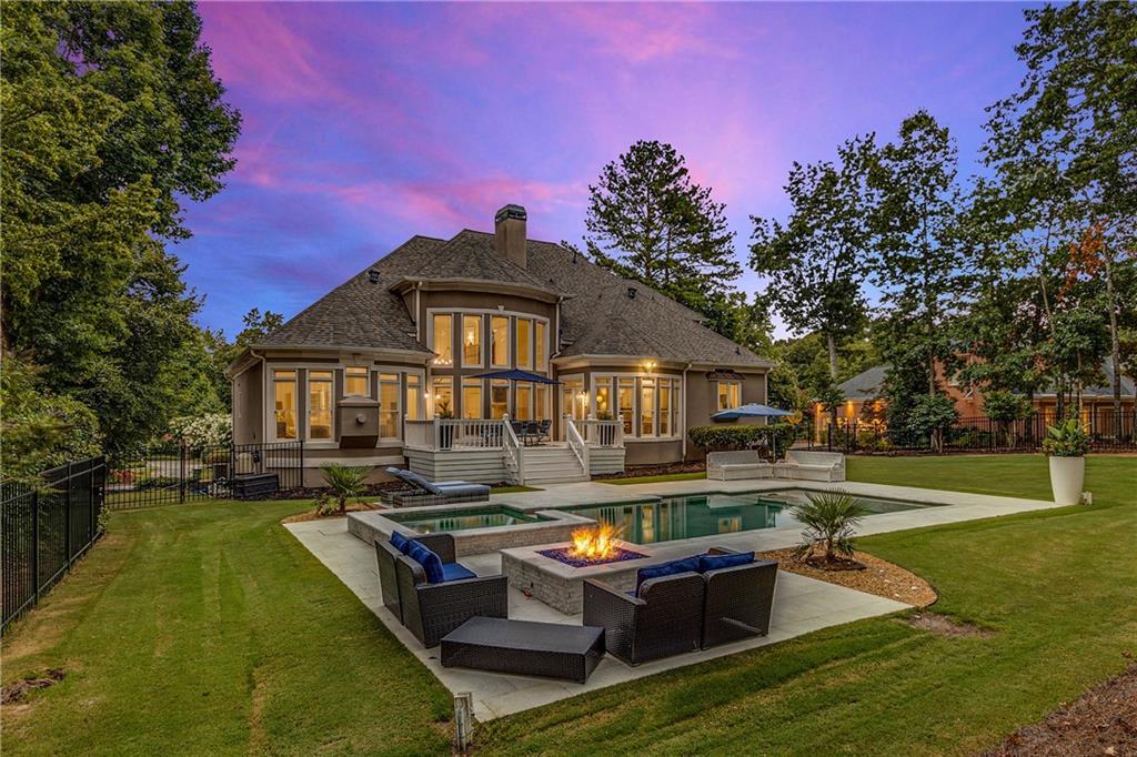 back house at dusk featuring a swimming pool with hot tub, a sunroom, a lawn, and a patio area