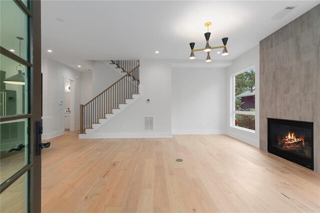 unfurnished living room with a chandelier, a wealth of natural light, a fireplace, and light hardwood / wood-style floors