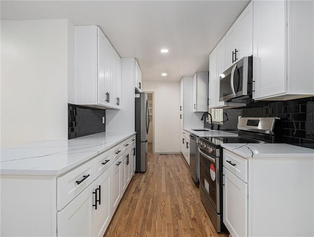 kitchen with a sink, light wood-style floors, white cabinetry, and stainless steel appliances