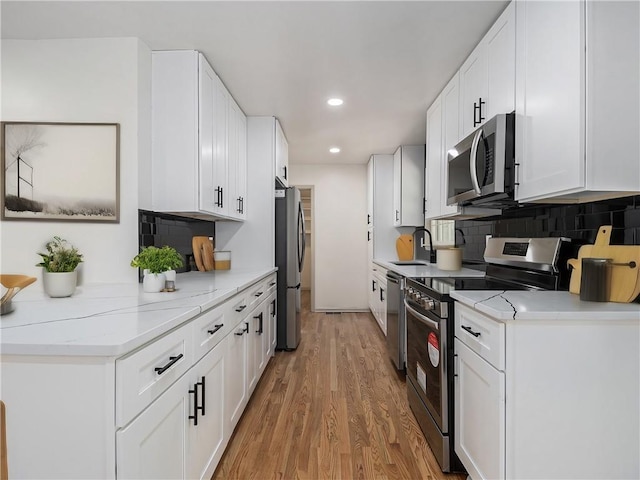 kitchen with light wood finished floors, backsplash, white cabinets, stainless steel appliances, and a sink