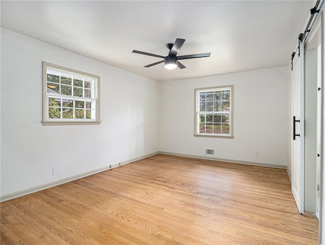 spare room with a barn door, visible vents, a wealth of natural light, and light wood-type flooring