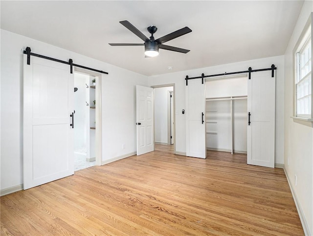 unfurnished bedroom featuring a barn door, light wood-style floors, baseboards, and ensuite bathroom