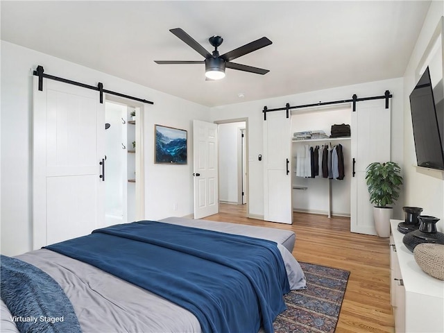 bedroom with a spacious closet, light wood-style flooring, a barn door, and ceiling fan