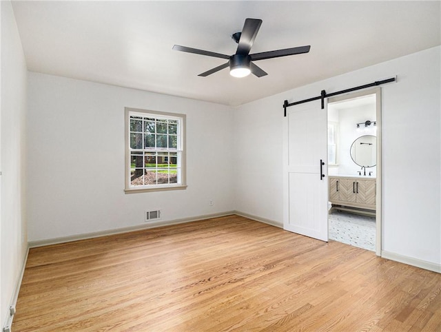 unfurnished bedroom with visible vents, a barn door, connected bathroom, light wood finished floors, and baseboards