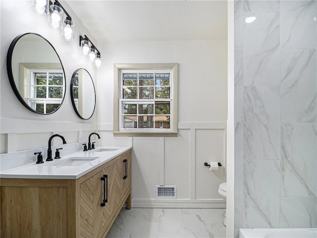 bathroom featuring visible vents, marble finish floor, a sink, wainscoting, and a decorative wall