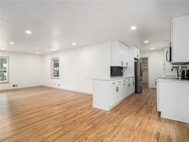 kitchen featuring appliances with stainless steel finishes, white cabinetry, light countertops, and light wood-style floors