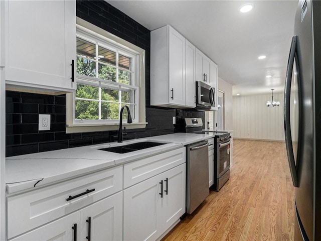 kitchen with a sink, white cabinets, light wood finished floors, and stainless steel appliances