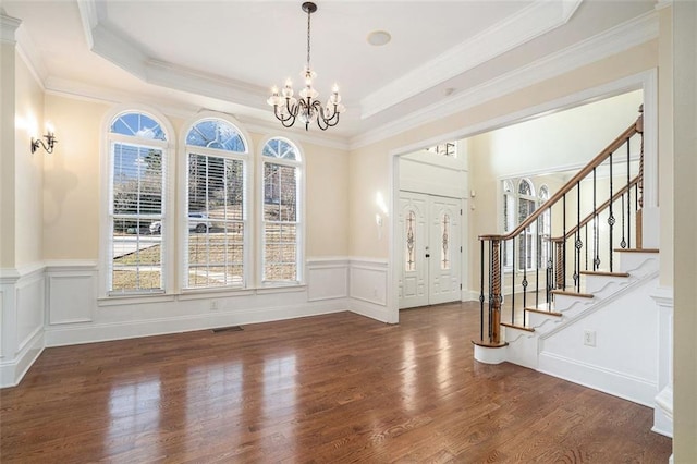 entryway with a tray ceiling, dark hardwood / wood-style floors, ornamental molding, and a chandelier