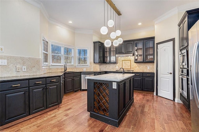 kitchen featuring decorative light fixtures, crown molding, a kitchen island with sink, stainless steel appliances, and light stone counters