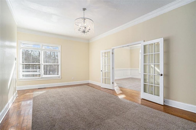 spare room with french doors, an inviting chandelier, ornamental molding, and hardwood / wood-style flooring