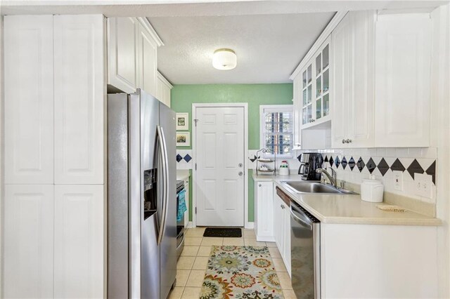 kitchen featuring backsplash, sink, light tile patterned flooring, stainless steel appliances, and white cabinets