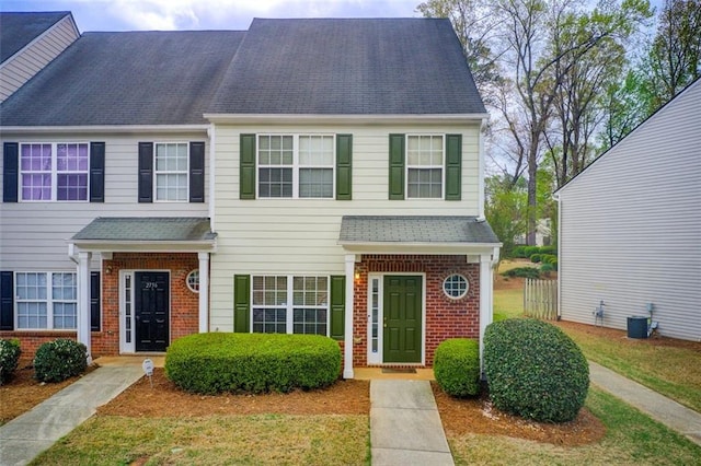 multi unit property featuring brick siding, cooling unit, and roof with shingles