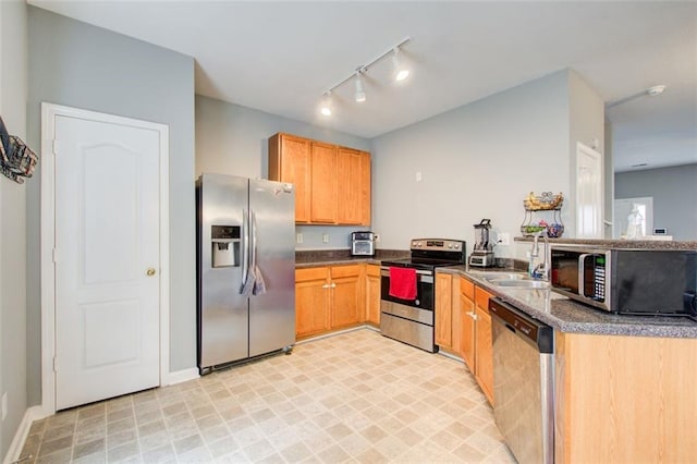 kitchen featuring rail lighting, light floors, appliances with stainless steel finishes, a sink, and dark countertops