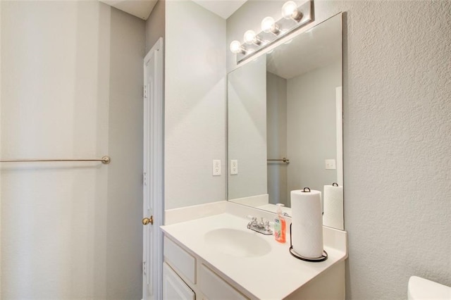 bathroom featuring toilet, vanity, and a textured wall