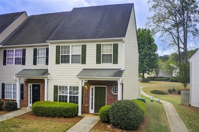 multi unit property featuring roof with shingles, brick siding, and a front lawn
