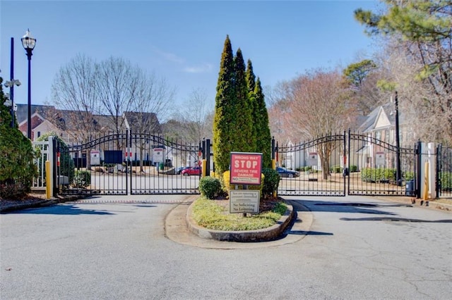 view of road featuring curbs, a gated entry, a gate, and street lights