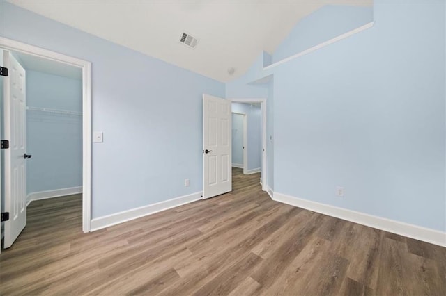 unfurnished bedroom with hardwood / wood-style floors, lofted ceiling, a closet, and a walk in closet