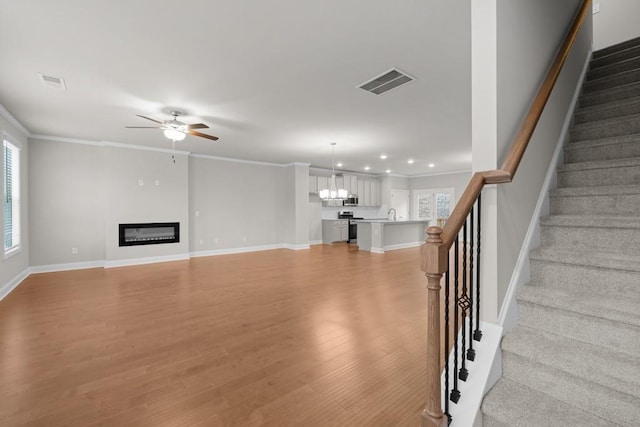 unfurnished living room featuring visible vents, light wood finished floors, stairs, and ceiling fan with notable chandelier