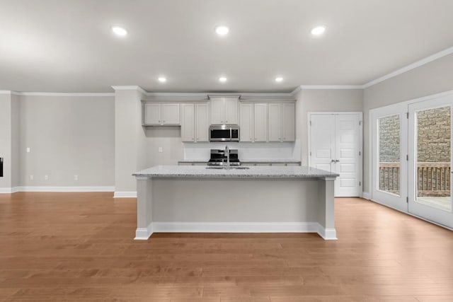 kitchen featuring stainless steel microwave, a kitchen island with sink, baseboards, and crown molding