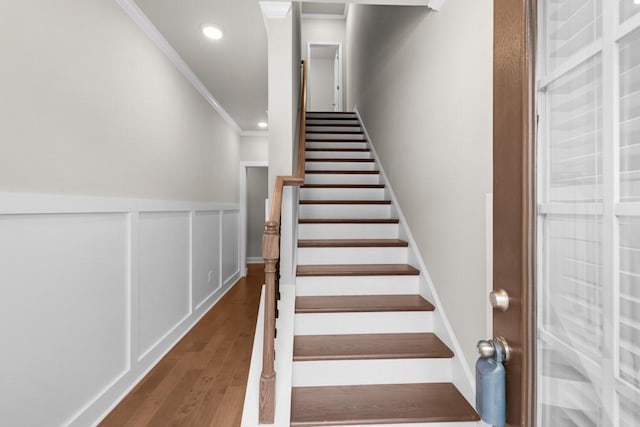 stairway featuring crown molding, wood finished floors, wainscoting, and recessed lighting