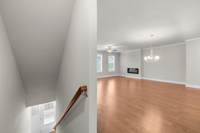 unfurnished living room featuring baseboards, ornamental molding, light wood-type flooring, ceiling fan with notable chandelier, and a glass covered fireplace