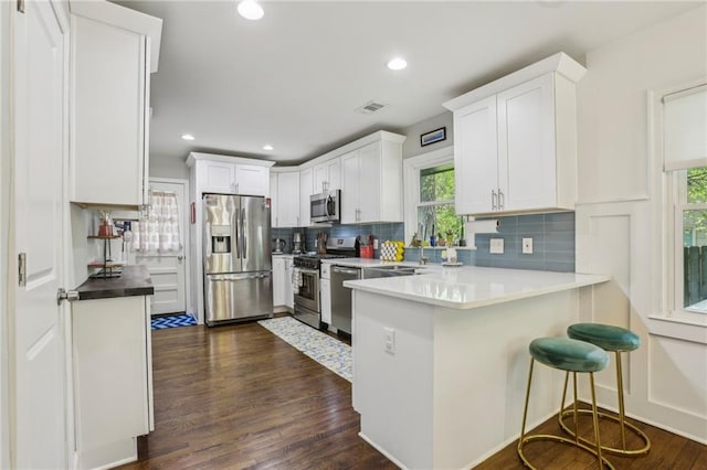 kitchen featuring dark wood finished floors, a peninsula, white cabinets, stainless steel appliances, and decorative backsplash