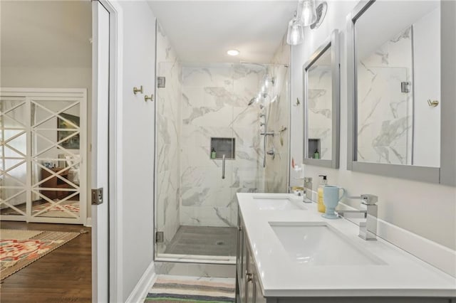 bathroom with a sink, a marble finish shower, double vanity, and wood finished floors