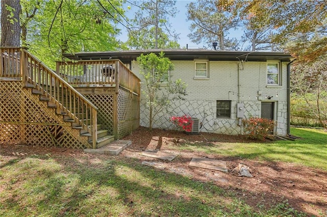 back of house featuring stairs, brick siding, a wooden deck, and a lawn
