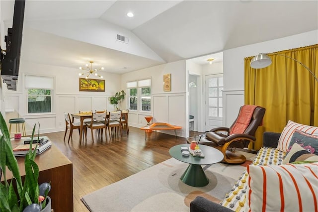 living area with a notable chandelier, vaulted ceiling, visible vents, a decorative wall, and wood finished floors