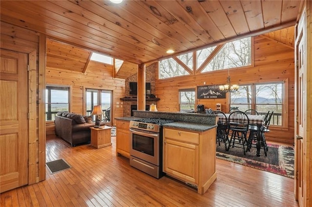 kitchen with a kitchen island, wooden walls, stainless steel gas range, an inviting chandelier, and light hardwood / wood-style flooring