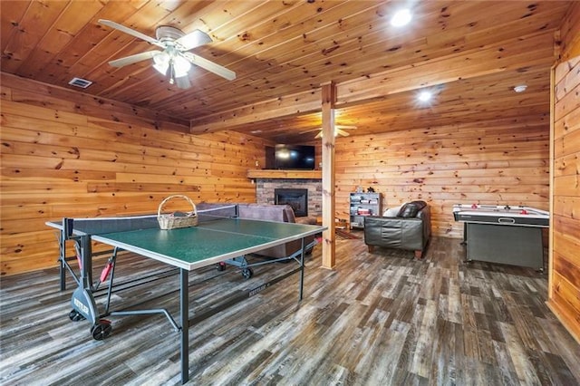 rec room with wood ceiling, a stone fireplace, dark wood-type flooring, and ceiling fan